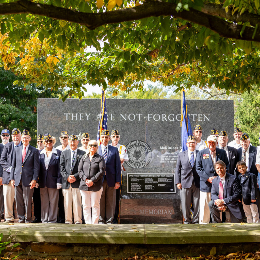 veterans standing in front of memorial black granite wall and flags
